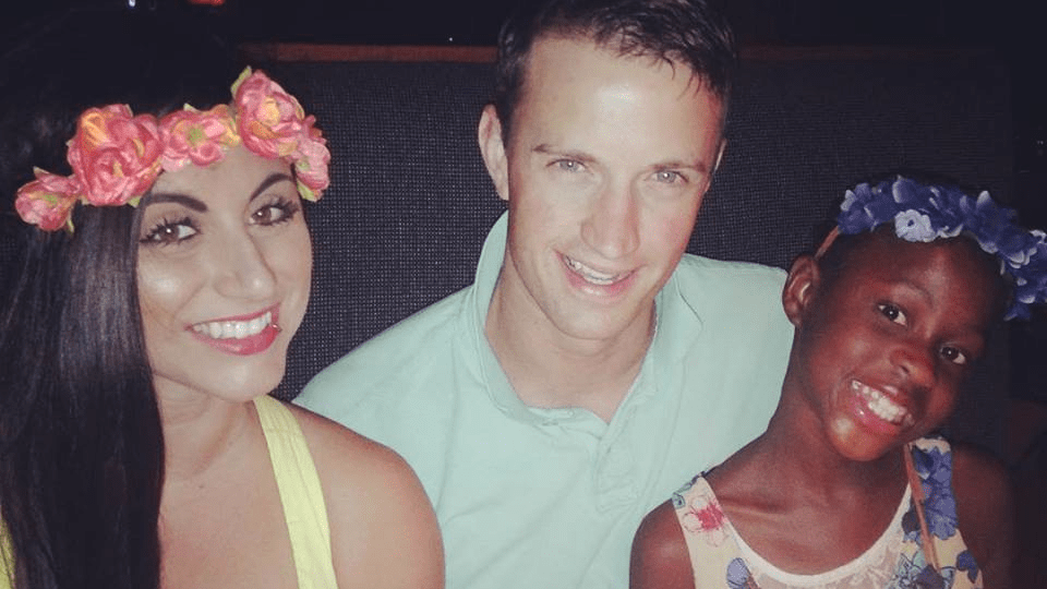 Pastor Elle, her husband Adam and her daughter smiles at the camera. Elle and Adam are white and have brown hair. Her daughter is Black and has black hair. All three are smiling.